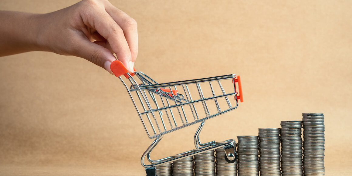 Grocery cart being pushed up a stack of coins. 